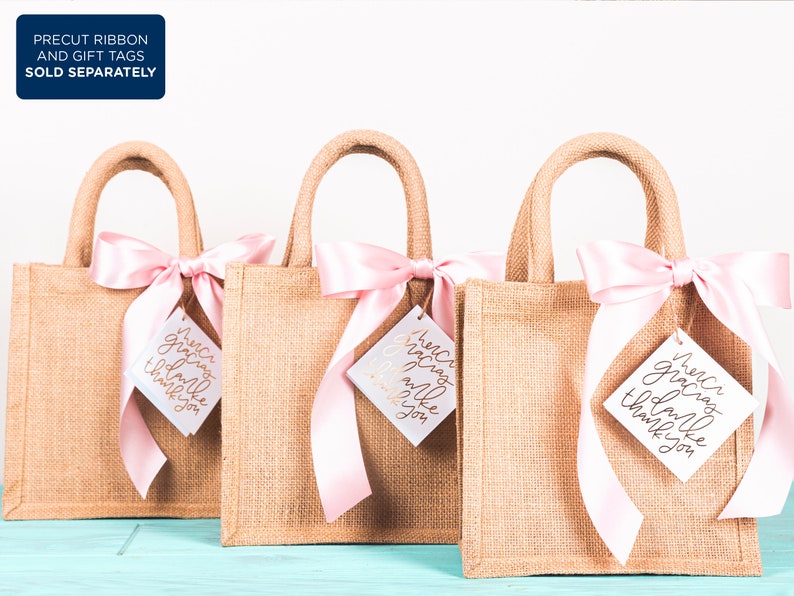 May include: Three small burlap gift bags with pink satin ribbon bows and white gift tags that say "Merci gracias thank you" in gold lettering.