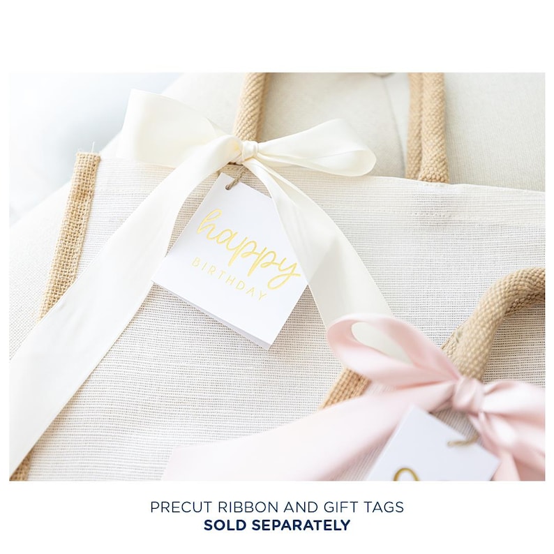 May include: Two natural burlap tote bags with white fabric lining. One bag is tied with a white satin ribbon and a white gift tag with gold lettering that says "happy birthday". The other bag is tied with a pink satin ribbon.