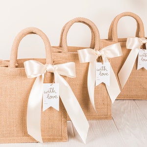 May include: Three brown burlap tote bags with white satin ribbon bows and white tags that say "with love".