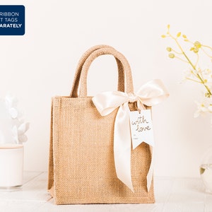 May include: A brown burlap tote bag with a white satin ribbon tied around the handles. The bag has a white gift tag attached to the ribbon that says "with love".
