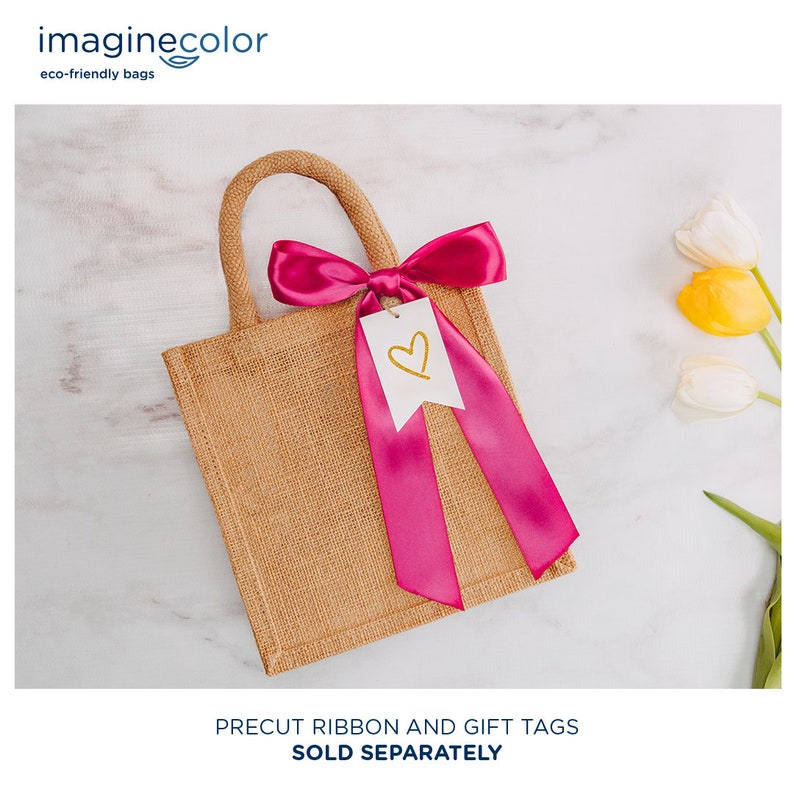 May include: A small, brown burlap tote bag with a pink satin ribbon tied in a bow and a white gift tag with a gold heart. The bag is on a white marble surface.