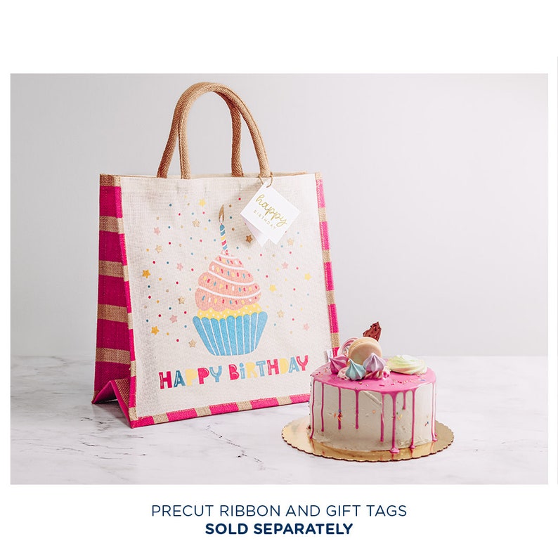 May include: A pink and white striped burlap tote bag with a cupcake design and the text "Happy Birthday". The bag is next to a pink and white frosted cake with a gold cake board.