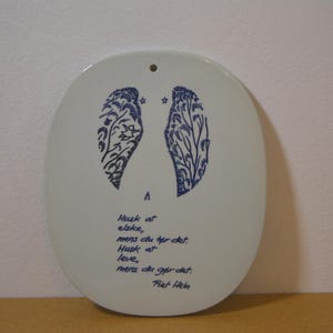 以下が含まれることがあります： 青い翼のようなデザインとテキストが施された、楕円形の白いセラミックウォールハンギング。 デザインは、花柄の2つの様式化された翼、2つの星、筆記体のテキストを特徴としています。 上部には吊り下げ用の小さな穴があります。