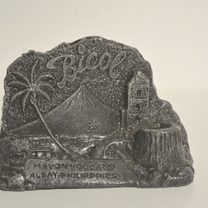 May include: A gray souvenir depicting the Bicol region in the Philippines. The design includes a volcano, palm trees, a church, and the text "Bicol" and "Mayon Volcano, Albay, Philippines."