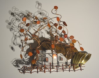 May include: A copper wire sculpture of a house with a thatched roof and a fence. The house is surrounded by a tree with copper leaves. The sculpture is mounted on a white wall.