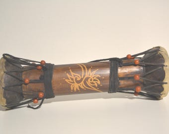 May include: A brown wooden drum with black and brown rope and red beads. The drum has a decorative design of a stylised flower.