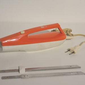 May include: A vintage electric knife with a white and orange handle and two serrated blades. The knife has a cord with a two-prong plug.