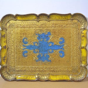 Op de afbeelding: Een rechthoekige decoratieve dienblad met een goudkleurig oppervlak en een blauw centraal ontwerp. De dienblad heeft een geschulpte rand en sierlijke details. De goudkleur heeft een verweerde uitstraling, wat bijdraagt aan de vintage charme.