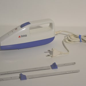 May include: A white and blue electric carving knife with two serrated blades. The knife has a handle and the brand name "SEB" printed on the side. The power cord is white and has a blue rubber band holding it together.