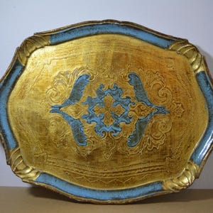 Könnte beinhalten: Dekorative Serviertablett in Gold mit hellblauem Rand und Zierdetails. Das Tablett hat ein zentrales Design in Hellblau und Gold, mit komplizierten Schnörkeln und einem detaillierten Muster. Es hat Griffe auf jeder Seite.