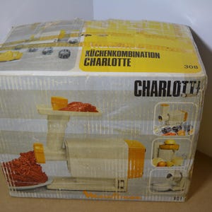 Könnte beinhalten: Eine Vintage-Küchengerätebox mit der Aufschrift "KüchenKombination Charlotte". Die Box zeigt eine Abbildung des Geräts mit einem Creme- und Orangeton und Text auf Deutsch. Die Box ist leicht abgenutzt.