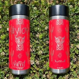 May include: Two red YETI Rambler 12 oz. tumblers with a Highland Cow and cactus pattern. The tumbler on the left has the name "Taylor" engraved on it.