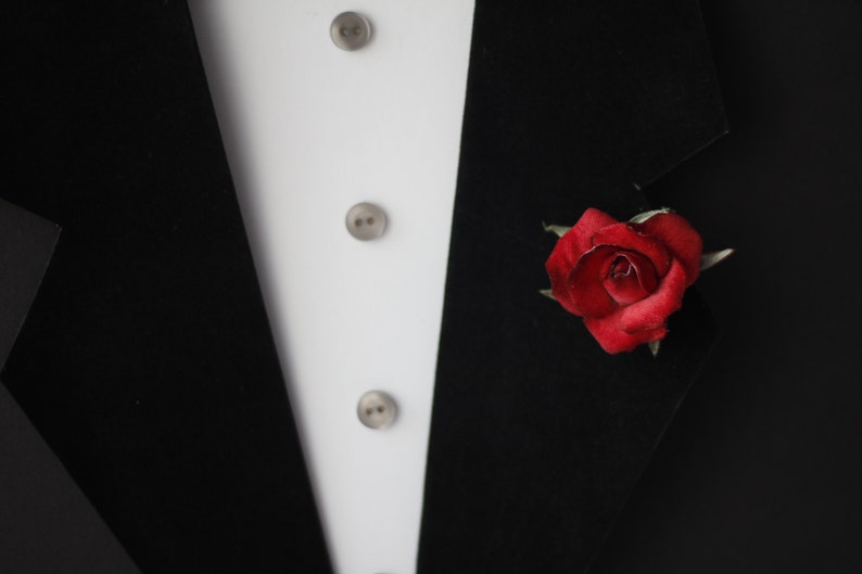 May include: A black tuxedo jacket with a white shirt and a single red rose boutonniere.