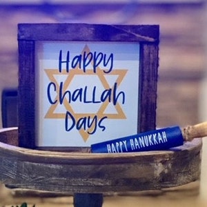 K&ouml;nnte beinhalten: Ein Holzschild mit dem Text "Happy Challah Days" und einem gelben Davidstern. Ein blauer Nudelholz mit dem Text "Happy Hanukkah" liegt auf einem Holztablett.