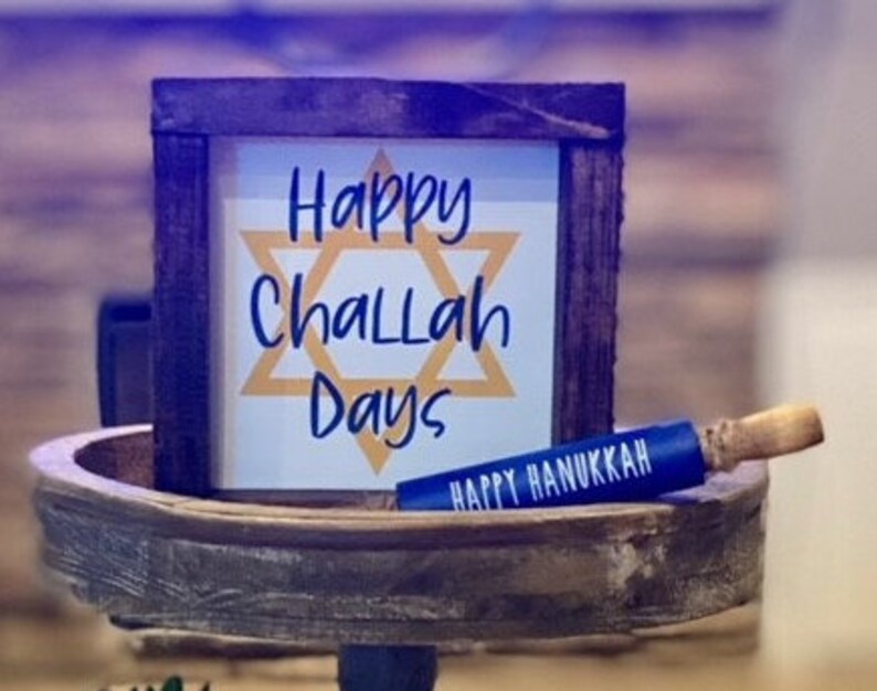 K&ouml;nnte beinhalten: Ein Holzschild mit dem Text "Happy Challah Days" und einem gelben Davidstern. Ein blauer Nudelholz mit dem Text "Happy Hanukkah" liegt auf einem Holztablett.