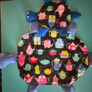 May include: A blue and black fabric turtle with a teacup pattern. The turtle has a smaller blue turtle on top of it. The teacups are in various colors and patterns.