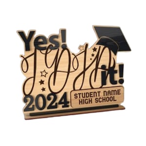 Peut inclure: Une pancarte de graduation en bois avec le texte "Yes! I Did It!" et l'ann&eacute;e "2024". La pancarte comprend &eacute;galement un bonnet de graduation noir et un espace pour le nom de l'&eacute;tudiant et le nom du lyc&eacute;e.