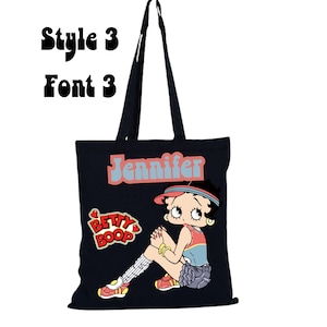 May include: Black canvas tote bag with a cartoon image of Betty Boop wearing a red and white baseball cap and a blue and white striped shirt. The bag has the name "Jennifer" printed in a retro font.