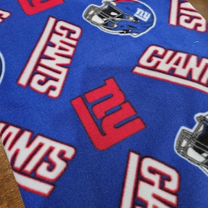 May include: A blue fleece fabric featuring a repeating pattern of the New York Giants logo, the word GIANTS in white letters with red outlines, and a blue football helmet graphic with the letters NY on the side in white and red.