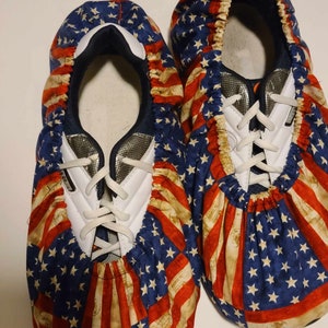May include: A pair of blue, red, and white shoe covers with a distressed American flag pattern. The shoe covers are made of fabric and have elastic around the top.