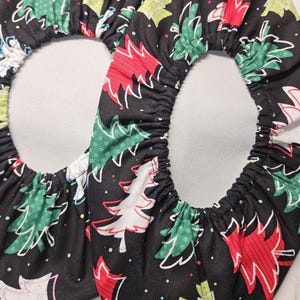 May include: A pair of round fabric bowl covers featuring a black background with a repeating pattern of stylized Christmas trees in red, green, and white, accented by small colorful dots. The covers have an elasticized edge for a snug fit.