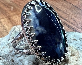 May include: A silver ring with a large oval blue agate stone set in a detailed silver filigree design.