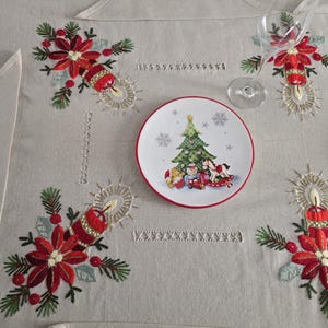 Könnte beinhalten: Ein beiger Weihnachtstischläufer mit gestickten roten Weihnachtssternen, Kerzen und grünen Tannennadeln. Ein Teller mit einem Weihnachtsbaum und Geschenken befindet sich in der Mitte. Weingläser und eine Serviette vervollständigen die festliche Szene.