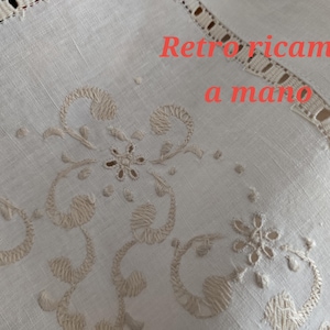 K&ouml;nnte beinhalten: Nahaufnahme eines cremefarbenen Textils mit aufwendigen gestickten Blumen- und Scrollwork-Designs. Der Text "Retro ricamo a mano" ist in Rot zu sehen. Die R&auml;nder weisen eine zarte, durchbrochene Bord&uuml;re auf.