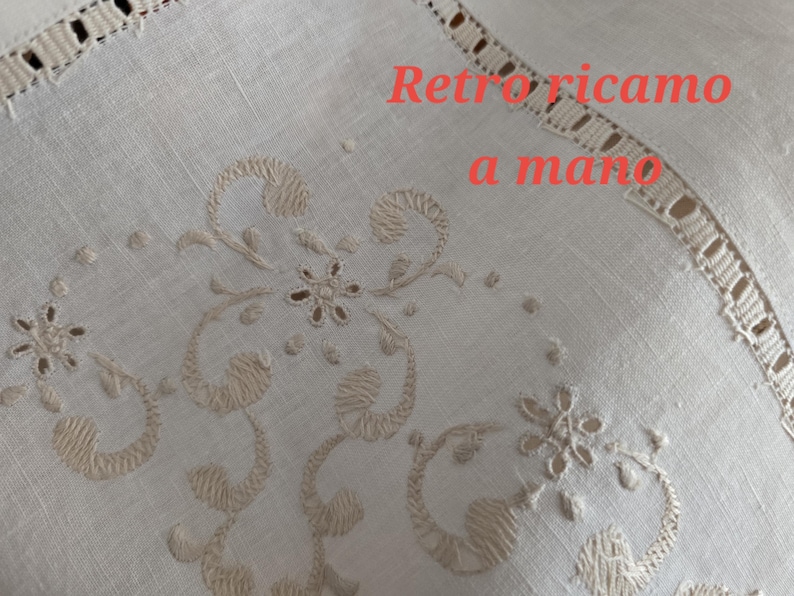 K&ouml;nnte beinhalten: Nahaufnahme eines cremefarbenen Textils mit aufwendigen gestickten Blumen- und Scrollwork-Designs. Der Text "Retro ricamo a mano" ist in Rot zu sehen. Die R&auml;nder weisen eine zarte, durchbrochene Bord&uuml;re auf.