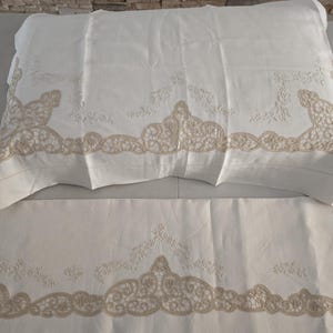 May include: White bedding set featuring a pillowcase and a sheet, both adorned with intricate beige lace detailing along the edges. The lace design adds a touch of elegance to the otherwise plain white fabric.