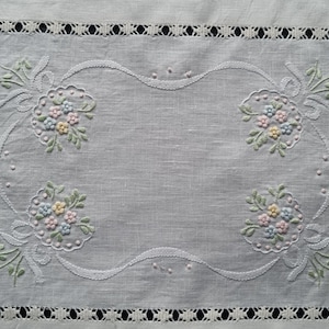 May include: White linen table runner with delicate embroidered floral designs in pastel colours. The runner features a scalloped edge and a lace border.