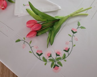 May include: A white tablecloth with pink embroidered flowers and green leaves. A bouquet of pink tulips is placed on the tablecloth.