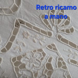 May include: Close-up of a white, hand-embroidered textile with cutwork details. The design features floral and geometric patterns, with the text "Retro ricamo a mano" in blue.