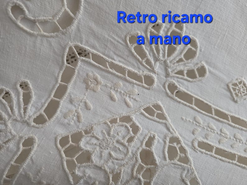 May include: Close-up of a white, hand-embroidered textile with cutwork details. The design features floral and geometric patterns, with the text "Retro ricamo a mano" in blue.