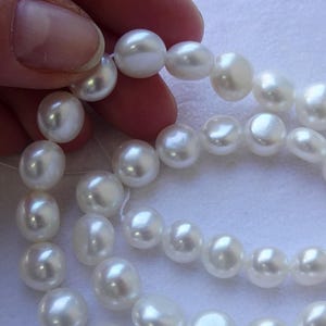 May include: A strand of white, lustrous, near-round freshwater pearls arranged in a loose spiral. Each individual pearl features a smooth, reflective surface with subtle variations in shape and size, strung together on a thin, clear filament thread.