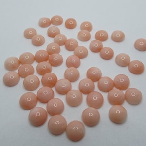 May include: A collection of round, pale pink cabochon gemstones. The stones are smooth and polished, with a slightly iridescent sheen.