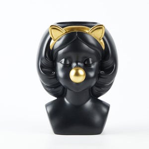 May include: Black decorative bust of a woman with a gold cat ear headband and a gold bubble. The bust has a round opening at the top and is set against a white background. The woman's hair is black and wavy.