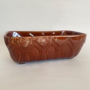 May include: A rectangular ceramic planter with a glossy brown glaze and a textured geometric diamond pattern along the exterior sides. The upper rim features a lighter, mottled brown finish, and the vessel has a deep, open interior cavity.