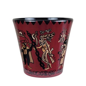 May include: A red ceramic cup with black rim and a black and white design of figures and symbols. The cup is decorated with a scene of people and animals.