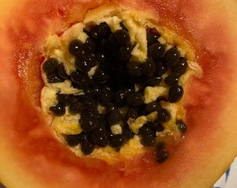 May include: A close-up of a papaya cut in half, revealing the black seeds inside. The papaya is ripe and has a bright orange flesh.