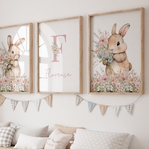 May include: Three framed prints featuring a watercolour illustration of a bunny holding a bunch of flowers. The middle print has the letter "F" and the name "Florence" in pink lettering.