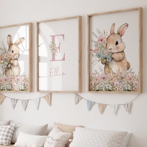 May include: Three framed prints featuring a watercolour illustration of a bunny holding a bunch of flowers. The middle print has the letter "E" and the name "Ellie" written in pink.