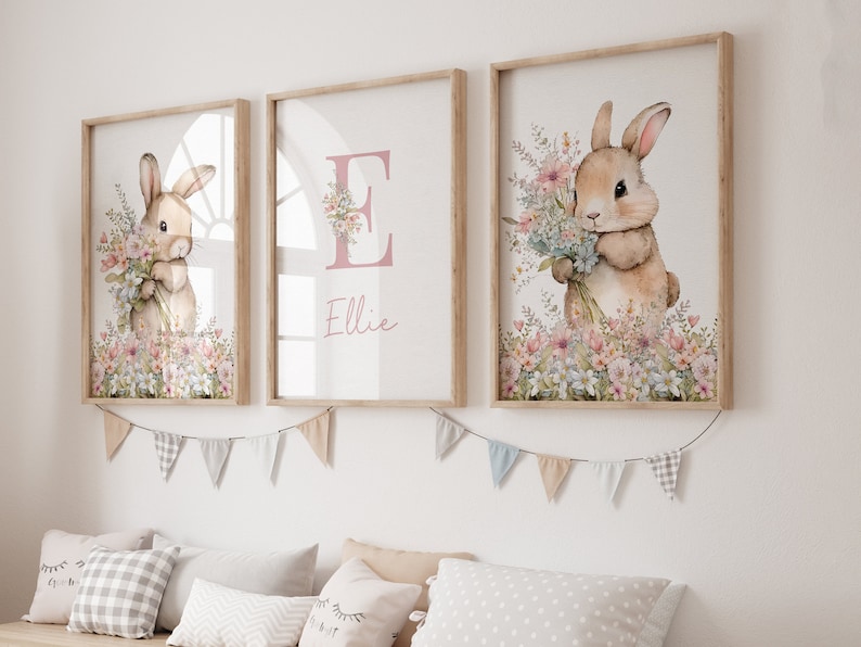 May include: Three framed prints featuring a watercolour illustration of a bunny holding a bunch of flowers. The middle print has the letter "E" and the name "Ellie" written in pink.