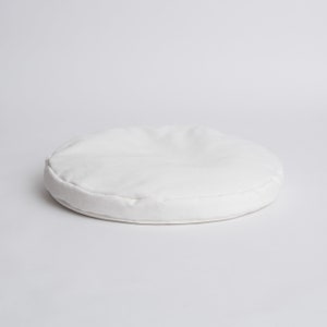 May include: A round, white cushion with a soft, fabric exterior. The cushion is circular, with a visible seam around the edge. The neutral color and simple design suggest a versatile home decor item, suitable for seating or decorative purposes.
