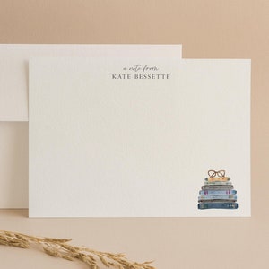 May include: A white card with the text "a note from KATE BESSETTE" printed in gray. A stack of books with a pair of glasses on top is illustrated on the right side of the card.