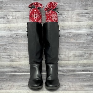 May include: A pair of black leather knee-high boots with a zipper on the side. The boots are standing upright with red and white bandana-style fabric stuffed inside.