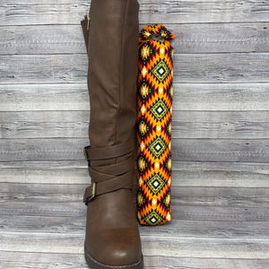 May include: A brown knee-high boot with buckle straps and a zipper, paired with two decorative boot shapers. The boot shapers feature a colorful geometric pattern in orange, yellow, green, and black, adding a vibrant contrast.