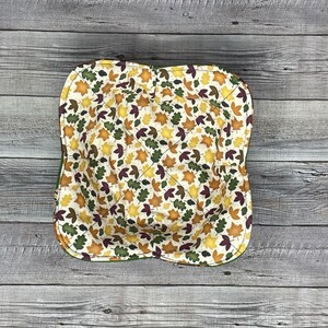 May include: A green fabric bowl with a white background and a pattern of fall leaves in shades of orange, yellow, brown, and burgundy.
