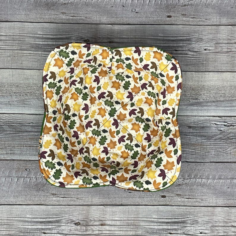 May include: A green fabric bowl with a white background and a pattern of fall leaves in shades of orange, yellow, brown, and burgundy.
