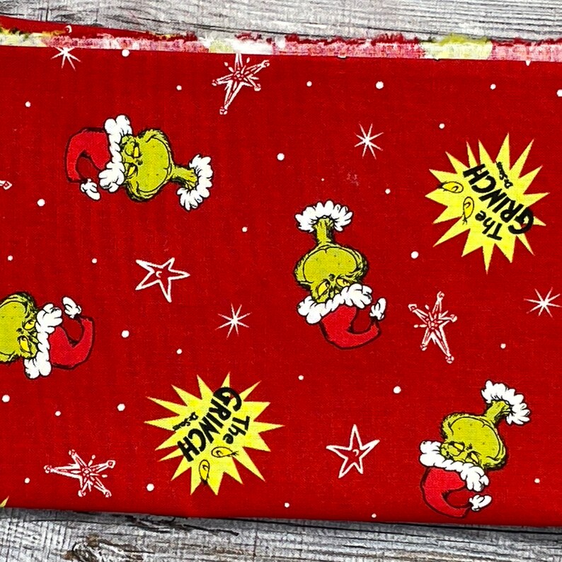 K&ouml;nnte beinhalten: Roter Stoff mit einem sich wiederholenden Muster aus dem Grinch mit einem Weihnachtsmann-Hut, einem gelben Stern mit dem Text "The Grinch" und wei&szlig;en Sternen.